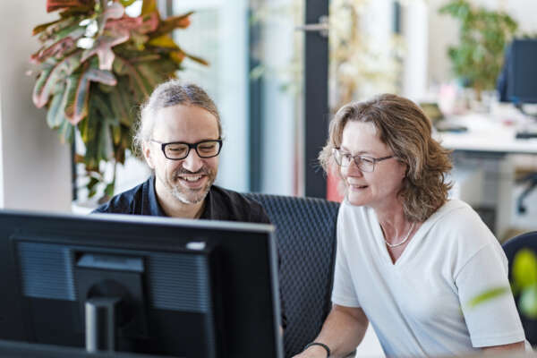 Zwei Personen in einem begrünten Büro vor einem PC.