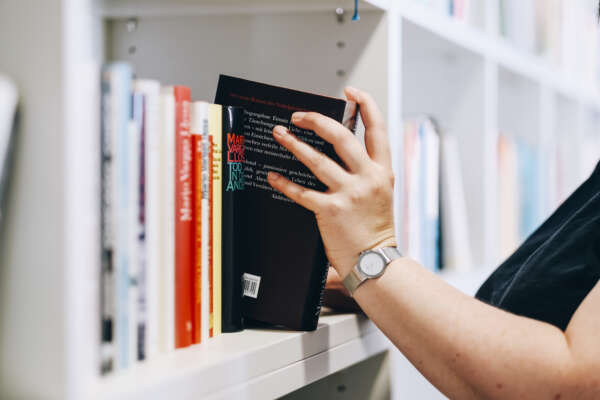 Eine Hand zieht ein Buch aus dem Regal.